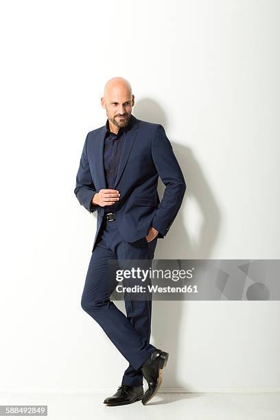 bald man with beard wearing blue suit standing in front of white background - blauw pak stockfoto's en -beelden