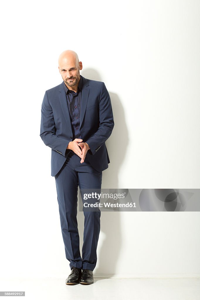 Bald man with beard wearing blue suit standing in front of white background