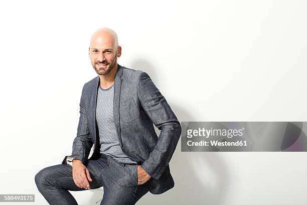 portrait of bald man wearing grey suit sitting in front of white background - three quarter length fotografías e imágenes de stock