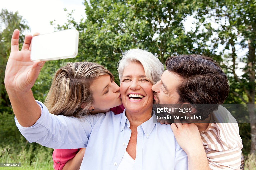 Happy mother with adult children taking cell phone picture outdoors