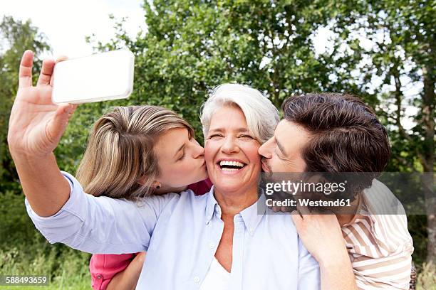 happy mother with adult children taking cell phone picture outdoors - sogra imagens e fotografias de stock