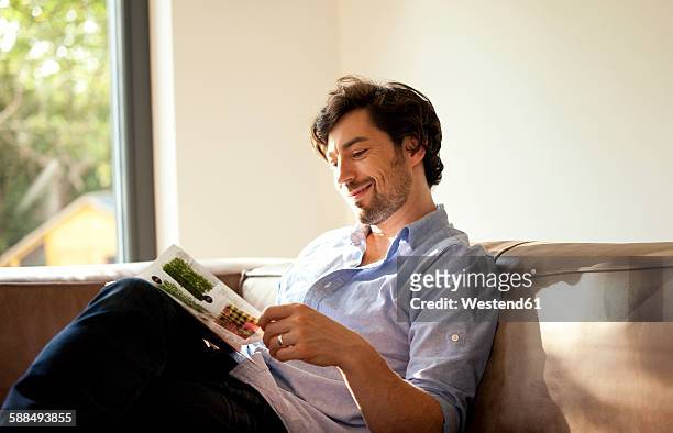 man sitting on couch reading catalogue - reading stock-fotos und bilder
