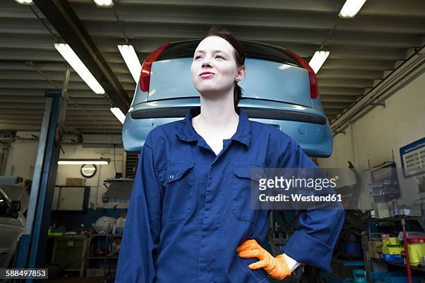 young woman working in repair garage, standing in front of hoist - issare foto e immagini stock