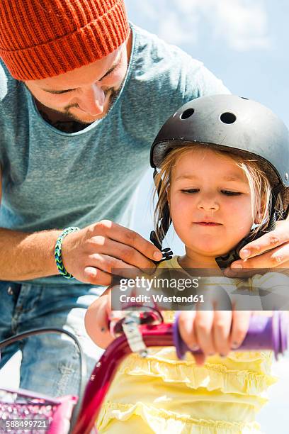 father closing daughter's helmet on bike - sports helmet fotografías e imágenes de stock