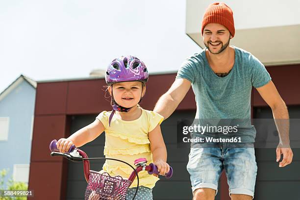 father supporting daughter on bike - ropa protectora deportiva fotografías e imágenes de stock