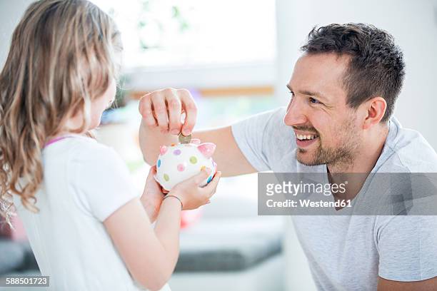 father and daughter throwing coin into piggy bank - allowance stock pictures, royalty-free photos & images