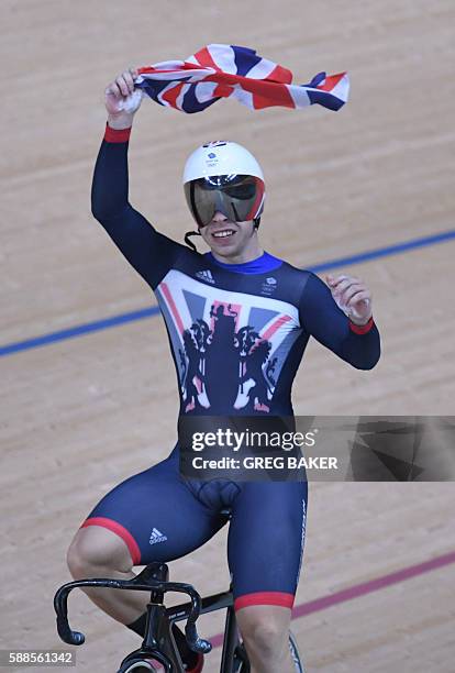 Britain's Philip Hindes holds up a flag as he celebrates after winning gold in the men's Team Sprint track cycling finals at the Velodrome during the...