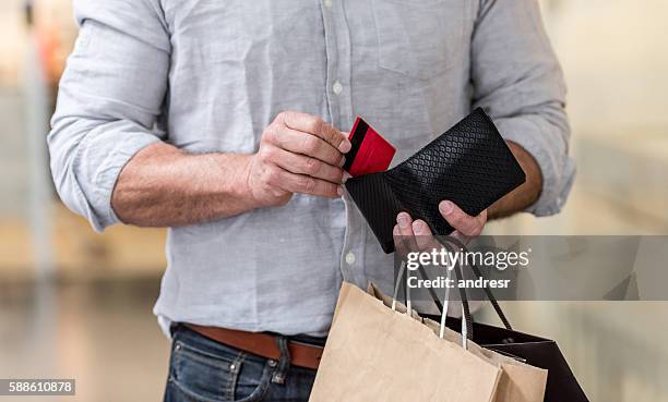 shopping man putting credit card in his wallet - spending money stockfoto's en -beelden