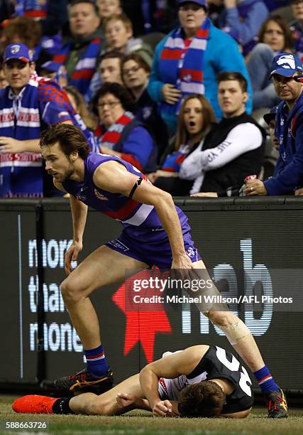 Darcy Moore of the Magpies lays injured after colliding with the fence as Joel Hamling of the Bulldogs looks on during the 2016 AFL Round 21 match...