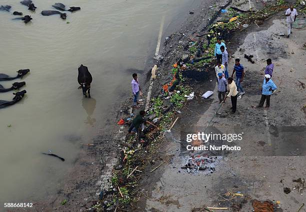 An indian dom cremates the dead body as mourn relatives stand near of cremation on the banks of flooded Ganges River , in Allahabad on August 12,2016.