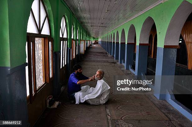 Kashmiri Muslim Gets his beard trimmed at a shrine during a curfew in Srinagar on August 11,2016.protests have entered second month in...