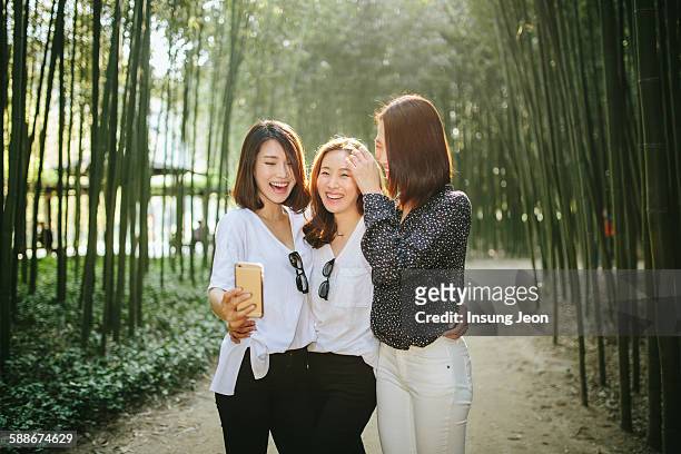 three young women taking photograph in park - young asian friends hugging stock-fotos und bilder
