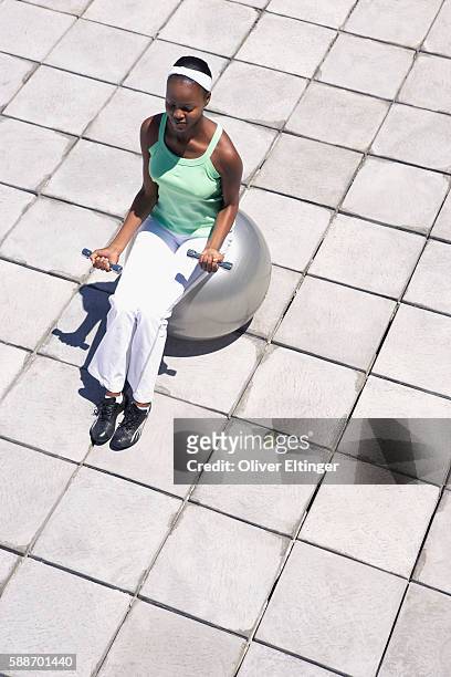 woman sitting on fitness ball lifting weights - oliver eltinger stock-fotos und bilder