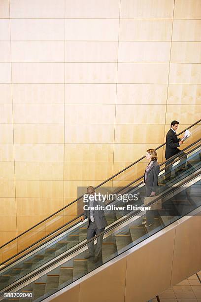 three businesspeople on escalators - oliver eltinger stock-fotos und bilder