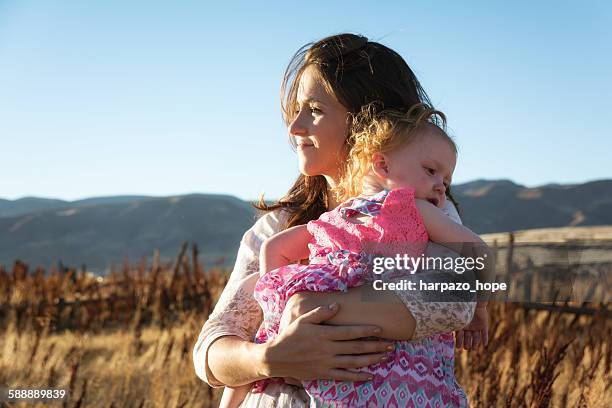 mother in a field holding her daughter - harpazo hope stock pictures, royalty-free photos & images