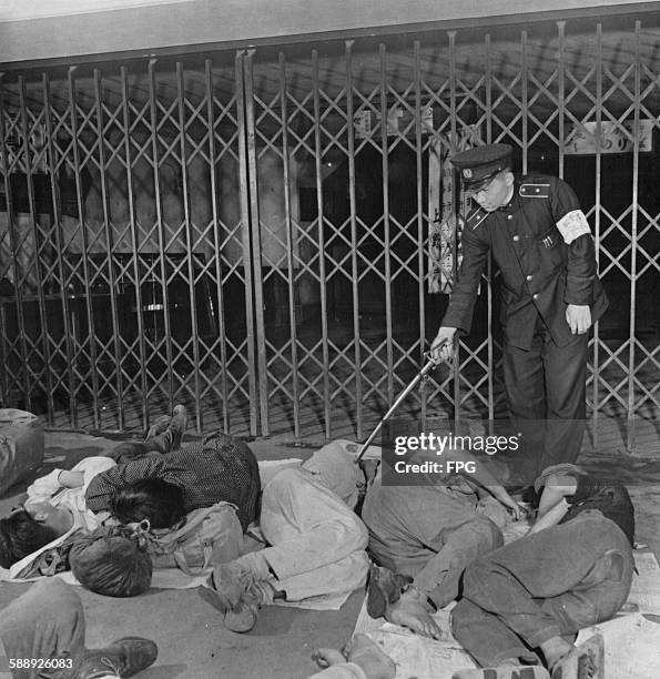 Policeman checks on the homeless people sleeping on the ground in Ueno Station, Tokyo, Japan, circa 1947.