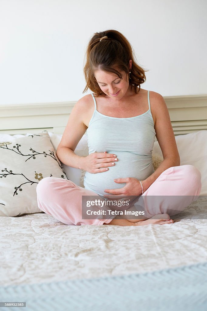 Smiling pregnant woman sitting on bed