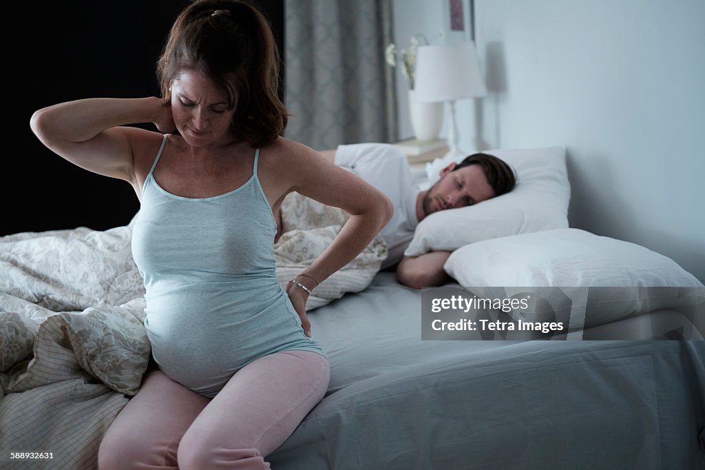 Woman sitting on bed and stretching stiff neck