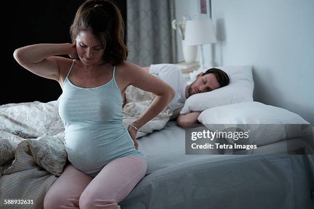 woman sitting on bed and stretching stiff neck - uncomfortable stock pictures, royalty-free photos & images