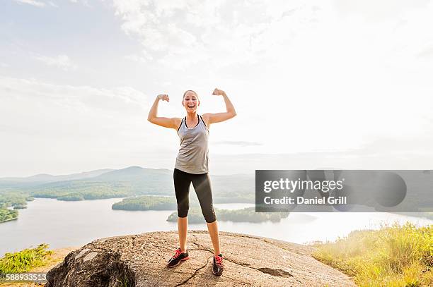 young woman standing on top of mountain and flexing muscles - flexing muscles stockfoto's en -beelden