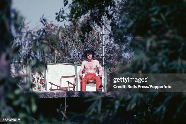 Scottish singer and guitarist Donovan pictured sitting in a chair and sunbathing at the Chaurasi Kutia ashram compound of Maharishi Mahesh Yogi near...