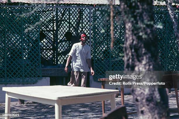 Paul McCartney from The Beatles pictured wearing red face paint as he walks through the Chaurasi Kutia ashram compound of Maharishi Mahesh Yogi near...