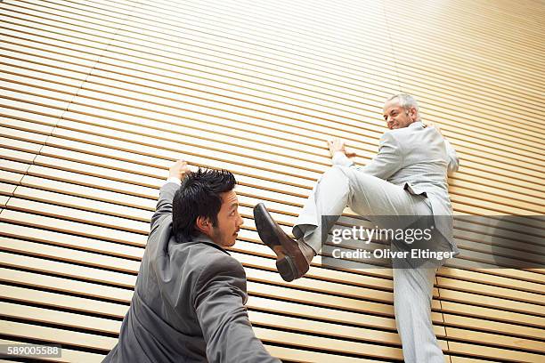 two businessmen fighting while climbing a wall - oliver eltinger - fotografias e filmes do acervo