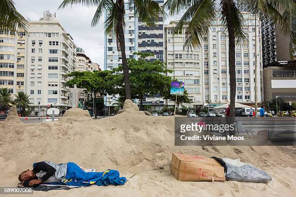 One or maybe two homeless or drunk man sleeping under a sand art statue of Christ with his arms outstretched, Christ the Redeemer, with elegant high...