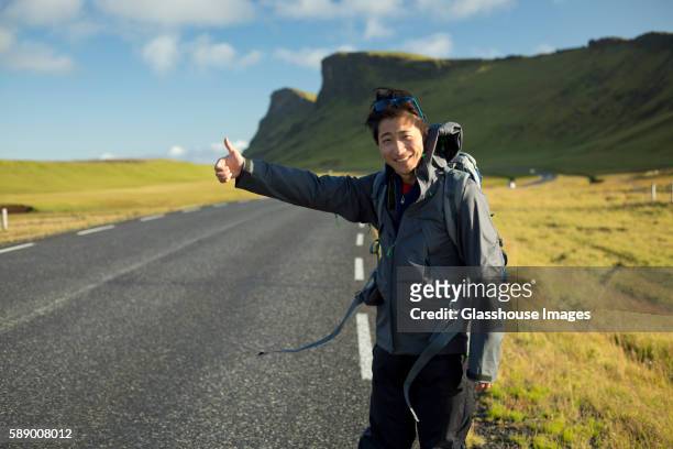 smiling young man hitchhiking along rural road - hitchhiking 個照片及圖片檔