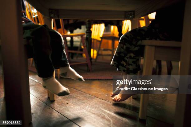 two young boy's feet underneath table - legs on the table foto e immagini stock