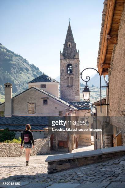 young adult woman walking through quaint village, rear view, lanslevillard, val cenis vanoise, france - steeple stock pictures, royalty-free photos & images