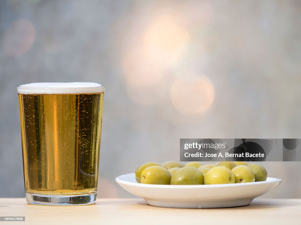 Glass of red wine and bowl of green olives on a wooden table outside, lit by sunlight