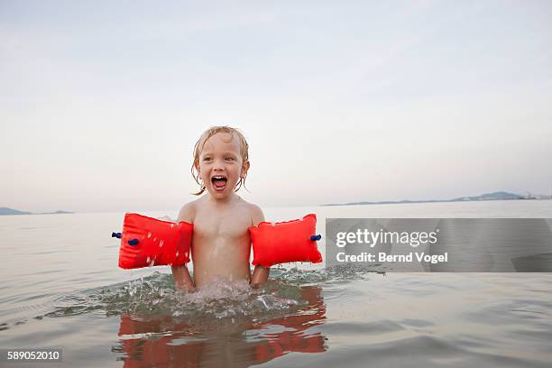 boy (7-9) with water wings swimming in lake - brazaletes acuáticos fotografías e imágenes de stock