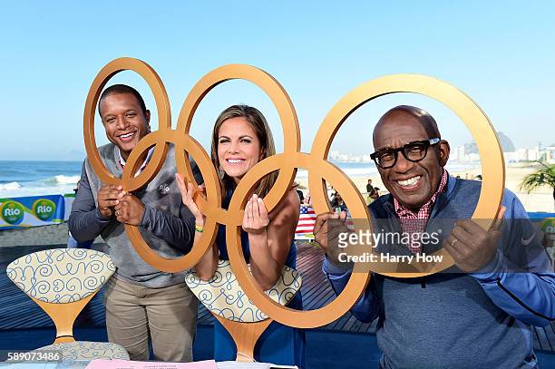 Hosts, Craig Melvin, Natalie Morales and Al Roker pose for a photo through Olympic rings on the Today show set on Copacabana Beach on August 13, 2016...