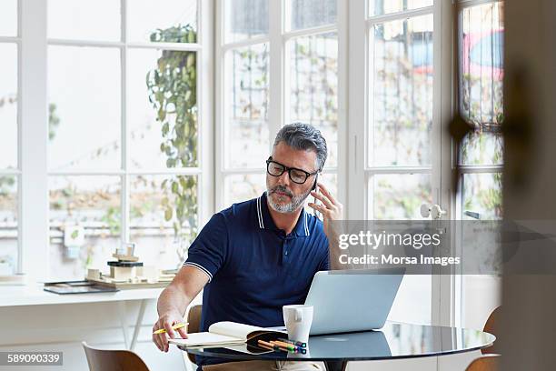 businessman using mobile phone while writing notes - mobile device on table stockfoto's en -beelden