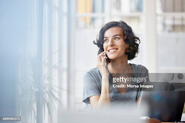 businesswoman using mobile phone in office - donna sorride cellulare foto e immagini stock