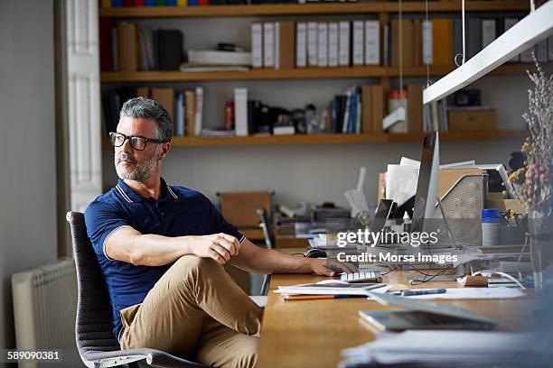 thoughtful businessman sitting at desk - regarder par dessus son épaule photos et images de collection