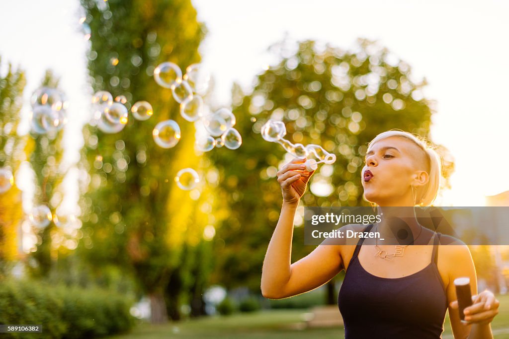 Bella bionda hipster che soffia bolle nel parco