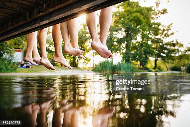 four young people sitting on a jetty - schommelen bungelen stockfoto's en -beelden