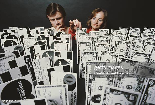 Man and a woman choose from an array of credit cards and dollar banknotes, 1979.