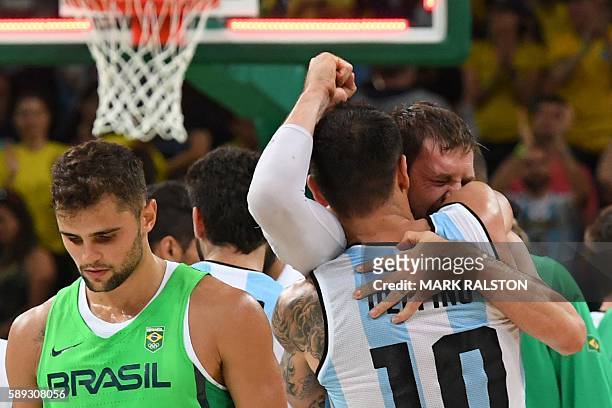 Argentina's shooting guard Carlos Delfino embraces Argentina's small forward Andres Nocioni as Brazil's point guard Raulzinho Neto walks by after...