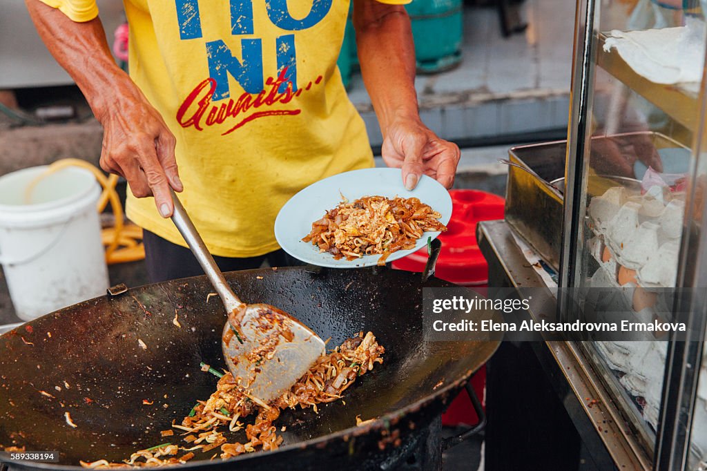 Hands of the senior man cooking kway teow noodles at the street market, Penang, Malaysia