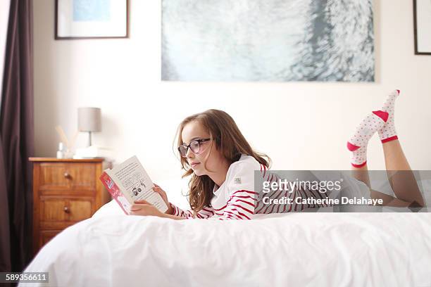 a 10 years old girl reading a book on her bed - 10 11 years ストックフォトと画像