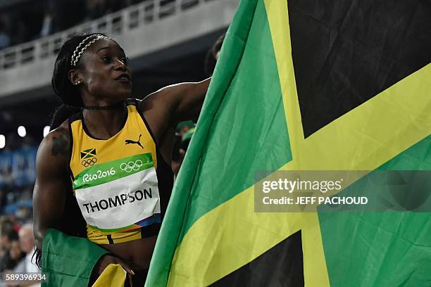 Jamaica's Elaine Thompson celebrates holding the Jamaican flag after she won the Women's 100m Final during the athletics event at the Rio 2016...