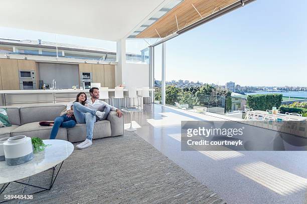 couple sitting in a modern open plan house. - luxury mansion interior stock pictures, royalty-free photos & images