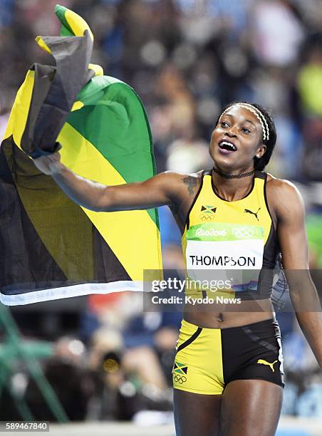 Jamaican sprinter Elaine Thompson holds the Jamaican national flag after winning the women's 100-meter final in the athletics competition of the Rio...