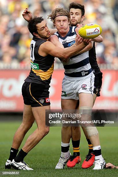 Josh Caddy of the Cats handballs as he is tackled by Shane Edwards and Trent Cotchin of the Tigers during the round 21 AFL match between the Richmond...