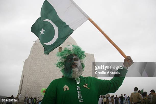 Pakistani man with his face painted in national colors holds a Pakistani flag during a ceremony marking Pakistan's 69th Independence Day at the...