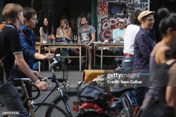 People sitting at an outdoor cafe in Oranienstrasse in Kreuzberg district watch as people demonstrating for women's rights walk past on a warm summer...