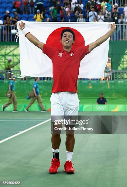 Kei Nishikori of Japan celebrates with the Japanese flag after winning the singles bronze medal match against Rafael Nadal of Spain on Day 9 of the...